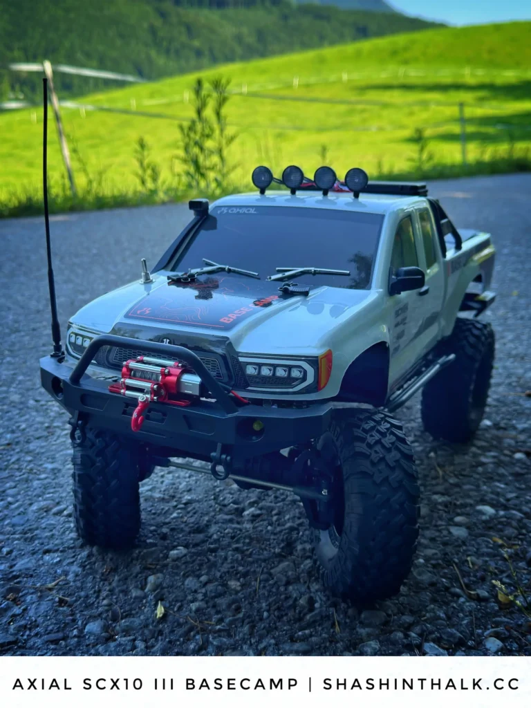 Axial SCX10 III Base Camp RC crawler on a gravel road with meadows behind